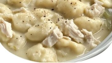A pot of Southern-style dumplings simmering in rich chicken broth, with soft dough pieces floating among shredded chicken.