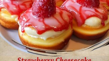 A close-up of strawberry cheesecake stuffed donuts, dusted with powdered sugar and oozing creamy cheesecake filling with chunks of strawberry.