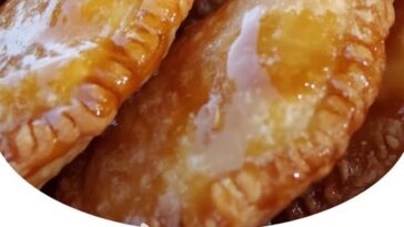 Golden, crispy hand pies stuffed with creamy cheesecake filling and spiced apples, with one pie cut open to reveal the gooey center.